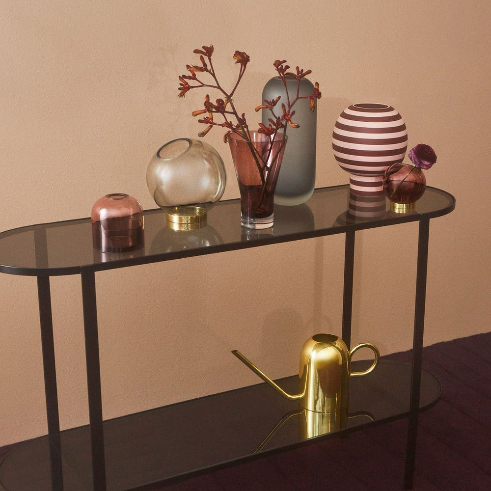 Modern decor featuring colorful vases in shades of pink, blue, and gold with stripes and smooth finishes on a dark tabletop.