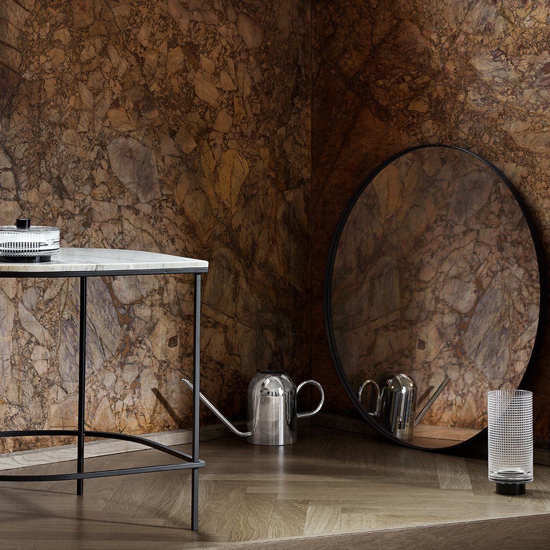 Round black mirror against a rich brown stone wall, complemented by a sleek white marble table and metallic accents.