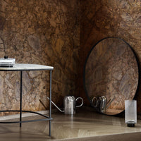 Round black mirror against a rich brown stone wall, complemented by a sleek white marble table and metallic accents.