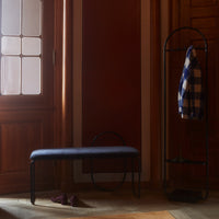 Navy blue bench against warm wooden tones, black accents, and a classic checkered coat hanging nearby.