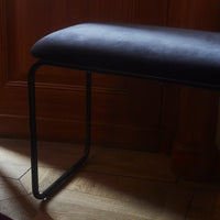 Black upholstered bench with a sleek metal frame, featuring a smooth, minimalist design against warm wood tones.