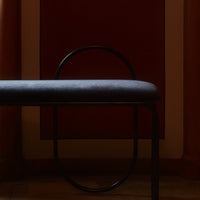 Gray upholstered bench with sleek black metal frame, set against a deep red wall. Minimalist, modern design.