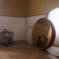 Round mirrors in warm amber and clear glass with sleek black geometric tables on a wooden floor. Elegant home decor.