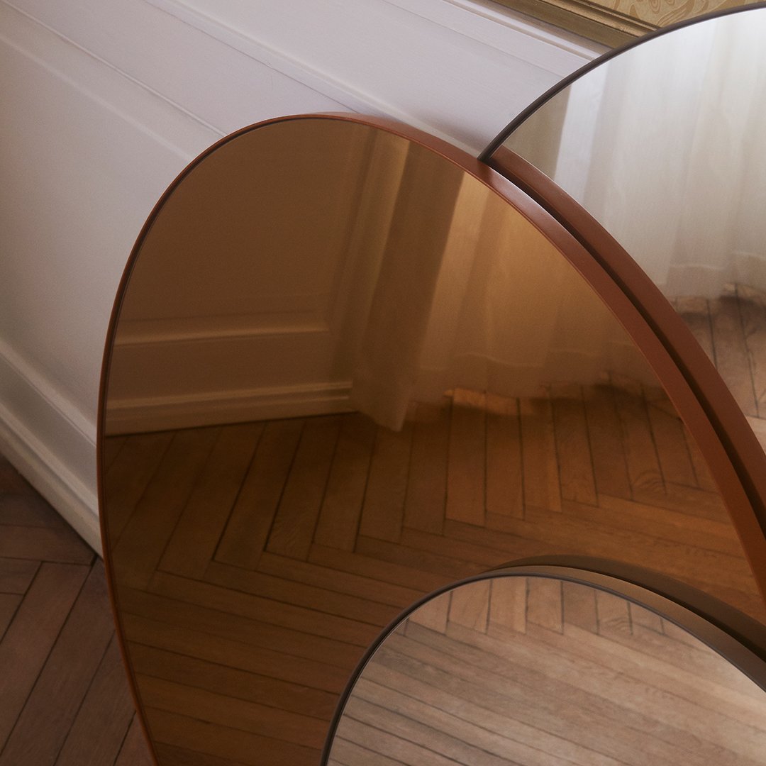 Modern brown-tinted glass table with smooth, rounded edges on a light wood floor background.