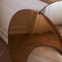 Modern brown-tinted glass table with smooth, rounded edges on a light wood floor background.