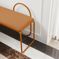 Modern bench featuring a warm, orange cushion with a sleek, curved metal frame on a marble floor.
