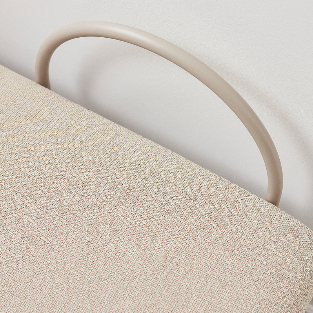 Beige textured fabric with a smooth, cream-colored curved handle. Soft, minimalist design detail.