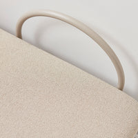 Beige textured fabric with a smooth, cream-colored curved handle. Soft, minimalist design detail.