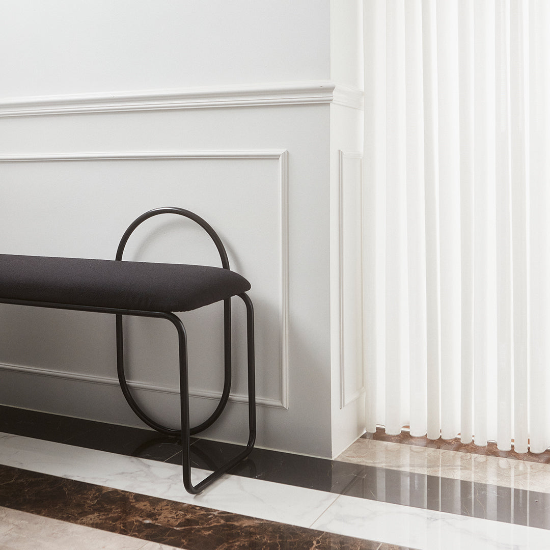 Modern black bench with a sleek curved design against a minimalist white wall and striped flooring in rich tones.