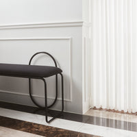 Modern black bench with a sleek curved design against a minimalist white wall and striped flooring in rich tones.