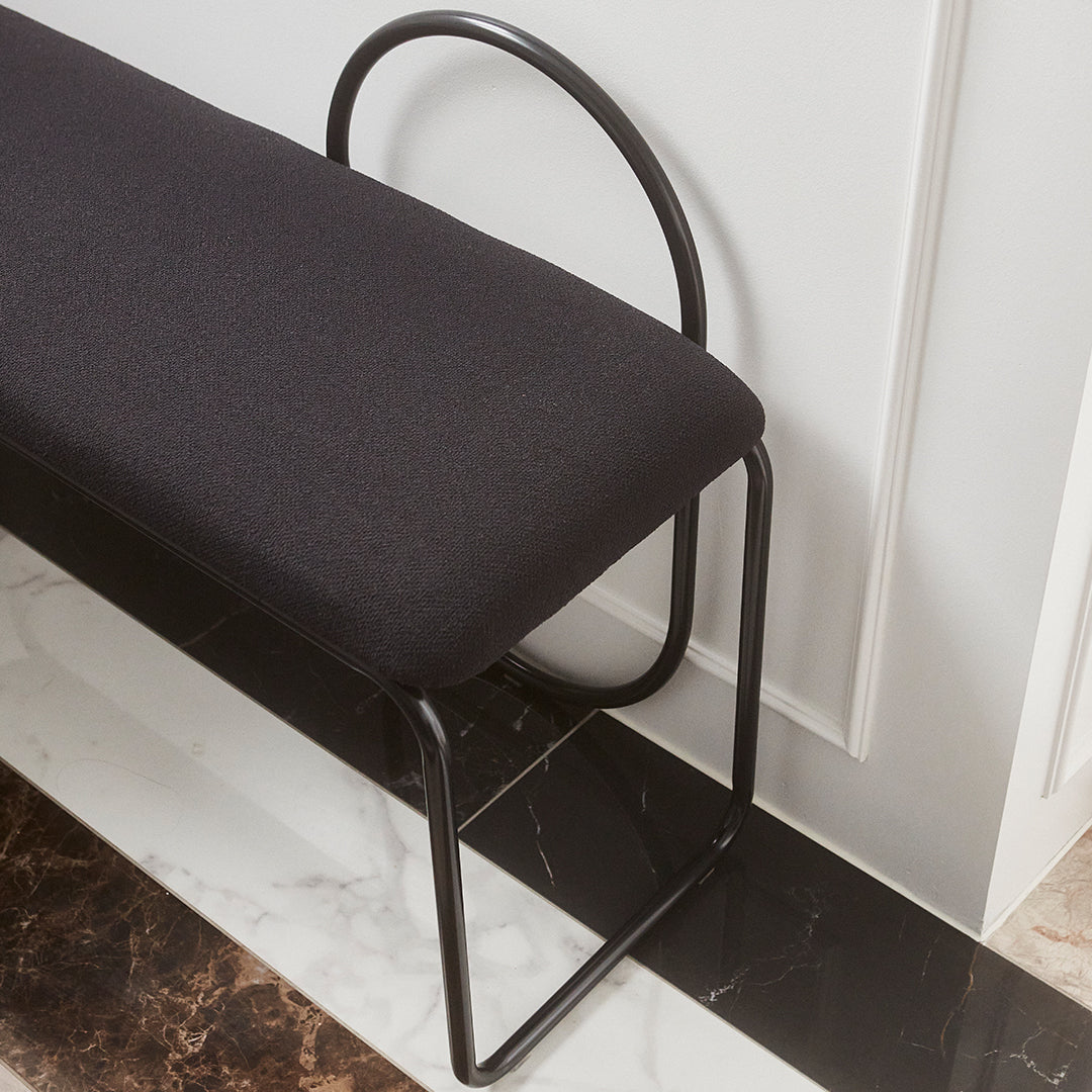 Black upholstered bench with sleek black metal frame on a white and dark marble floor. Modern minimalist design.