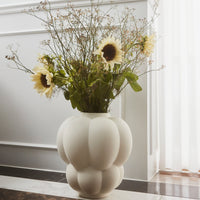 White textured vase with circular patterns, filled with sunflowers and greenery, set against a light, airy background.