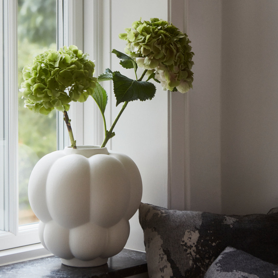 White textured vase with green hydrangea flowers, set against a cozy gray and black patterned backdrop.