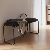 Black bench with soft upholstery and an abstract patterned throw blanket in neutral tones, set against a light wooden floor.