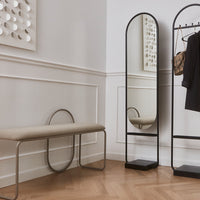 Beige bench with black metal frame, sleek mirror, and warm wooden floor accents in a modern interior.