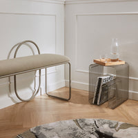 "Beige upholstered bench with curved metal legs, paired with a sleek wire side table and a patterned round rug."