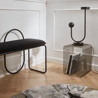Black upholstered bench with curved black metal frame, paired with a geometric wire side table and a patterned rug.