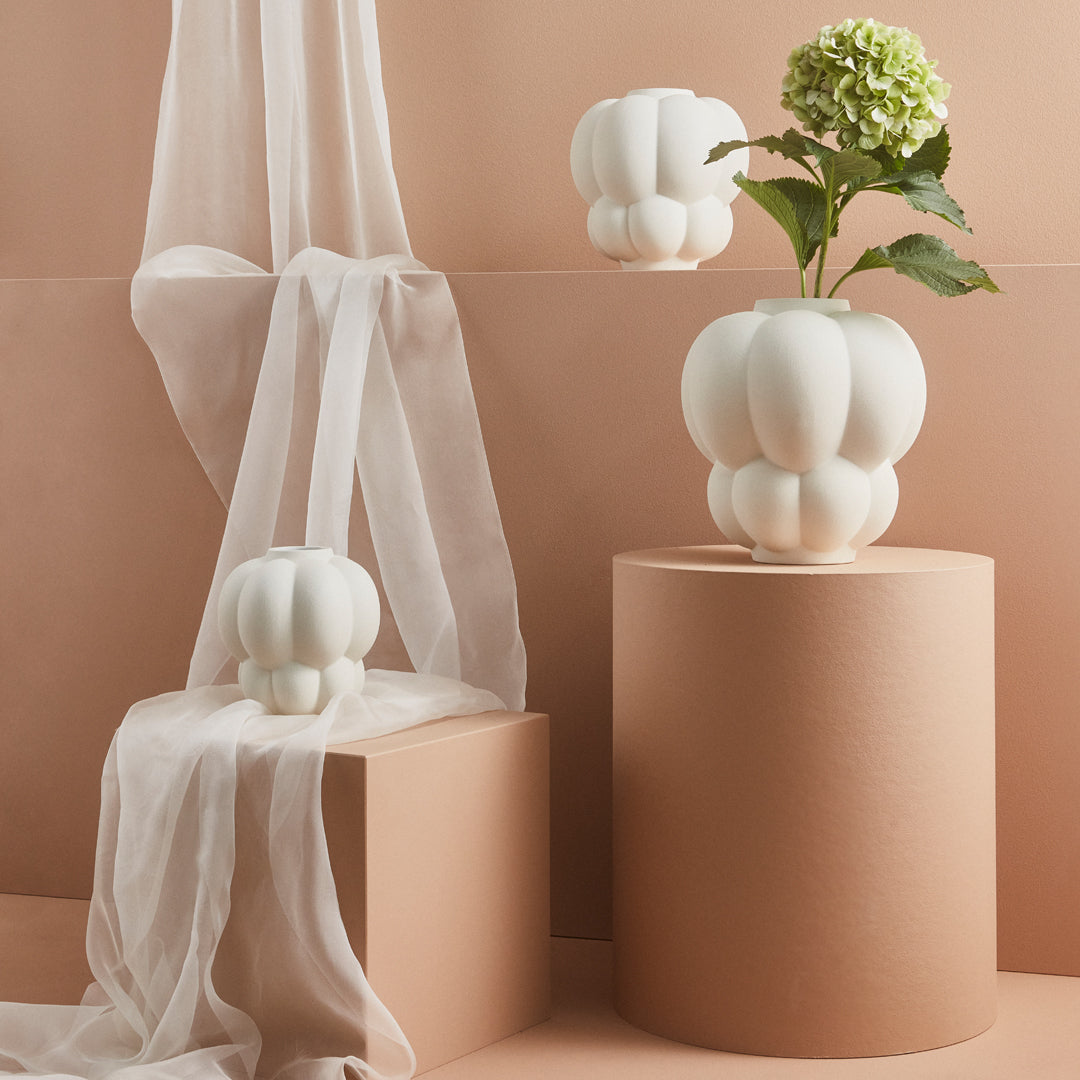 "Elegant white ceramic vases with a textured, rounded design against a soft peach backdrop and sheer fabric."