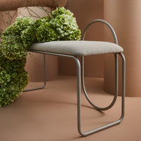 Gray upholstered bench with curved metal frame, surrounded by lush green hydrangeas against a warm brown backdrop.