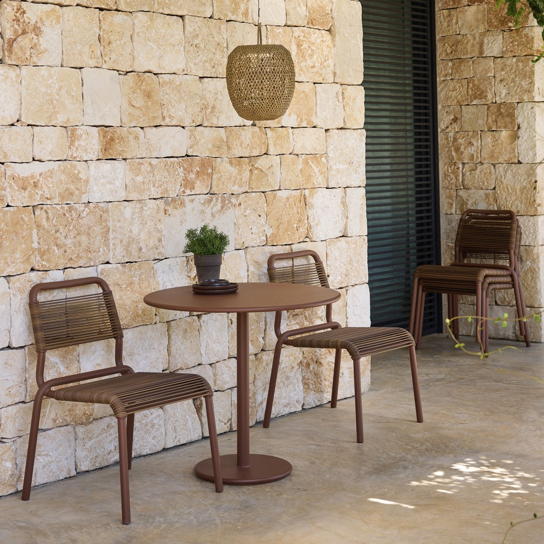 "Rustic brown bistro set with woven patterns, complemented by natural stone wall and greenery in outdoor setting."