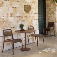 "Rustic brown bistro set with woven patterns, complemented by natural stone wall and greenery in outdoor setting."