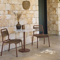 Brown chairs with woven patterns and a white marble table against a textured stone wall, creating a modern outdoor setting.