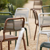 Colorful outdoor chairs in brown, green, white, and striped patterns, arranged on a sandy pathway.