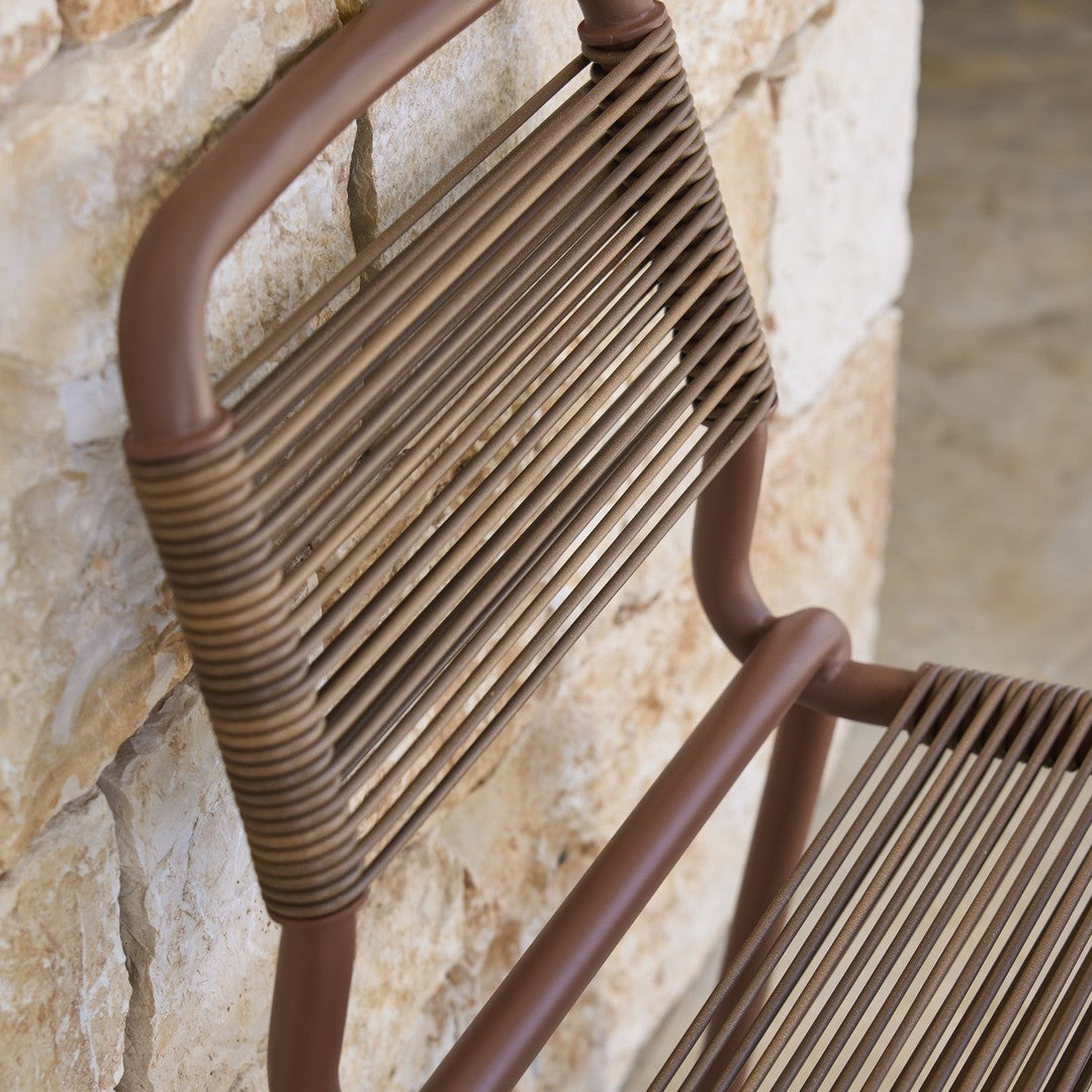 Brown woven rattan chair backrest against a textured stone wall, showcasing a horizontal stripe pattern.