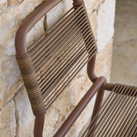 Brown woven rattan chair backrest against a textured stone wall, showcasing a horizontal stripe pattern.