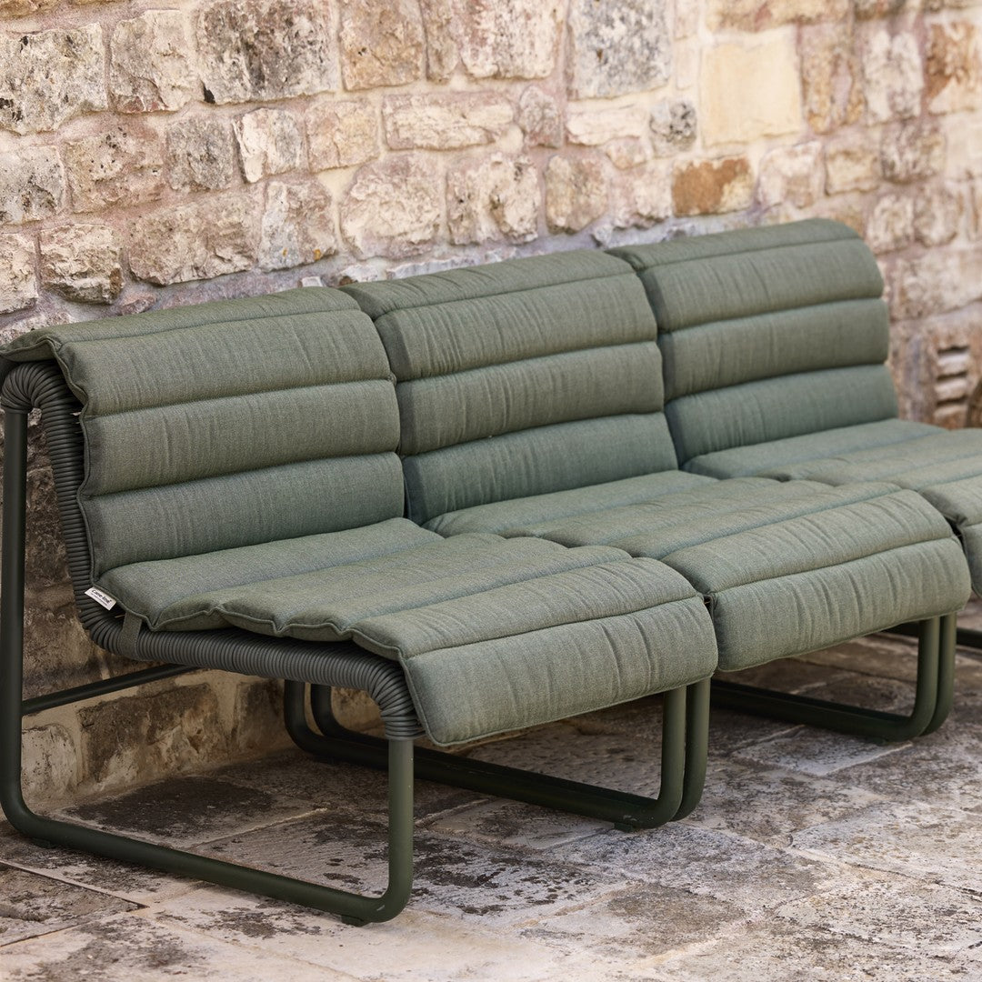 Olive green padded sofa with a sleek fabric design and modern metal frame against a rustic stone wall.