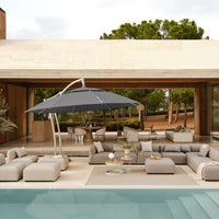 Gray outdoor umbrella over light beige lounge furniture by a pool, with neutral tones and natural textures in a modern setting.