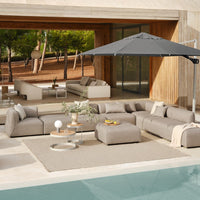 Luxurious outdoor sectional sofa in soft beige with gray accents, paired with a sleek gray umbrella and neutral rug.