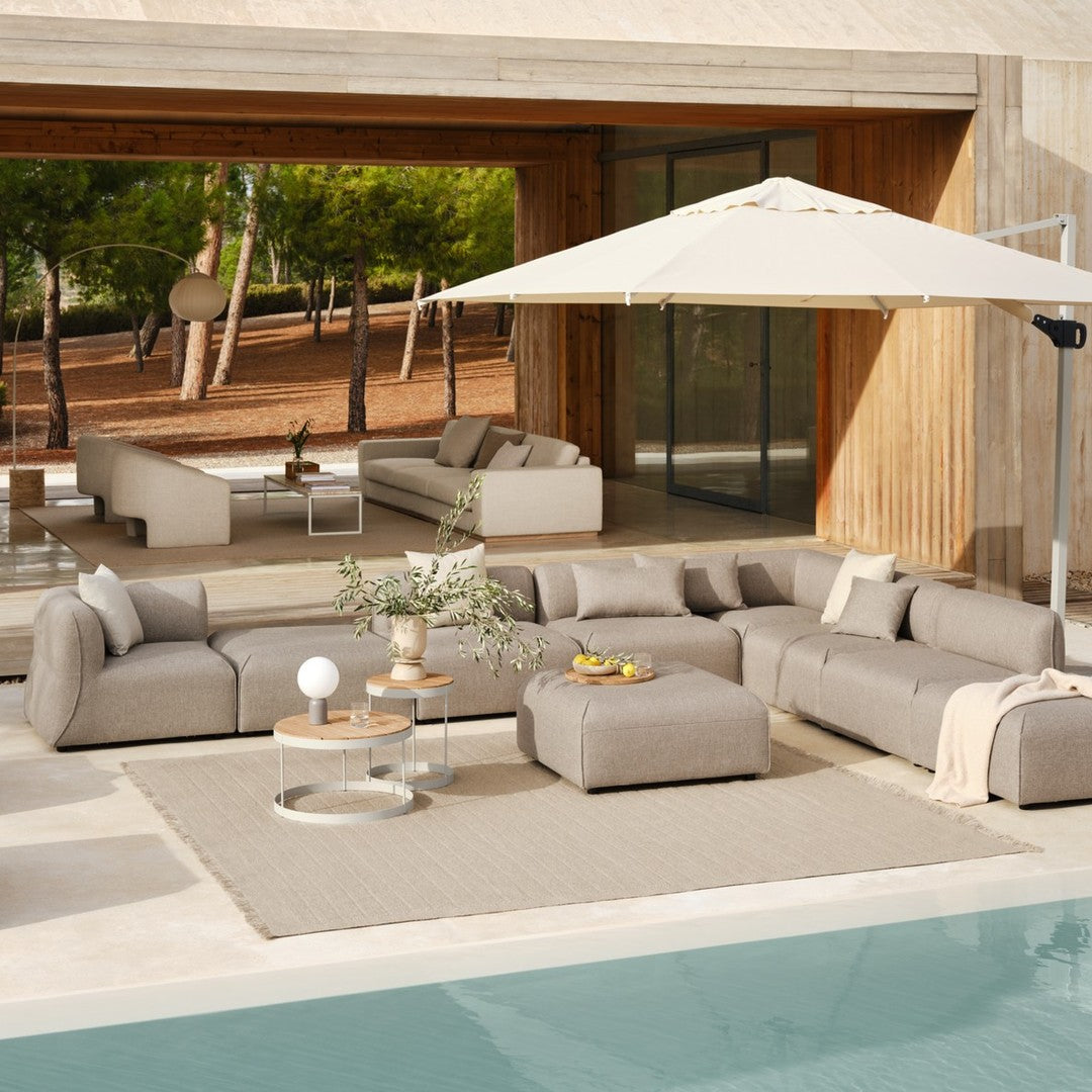 Elegant beige outdoor sectional sofa with textured cushions and cream umbrella against a modern, natural backdrop.