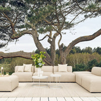 Beige modular outdoor sofa with plush cushions, set against a backdrop of greenery and natural wood tones.