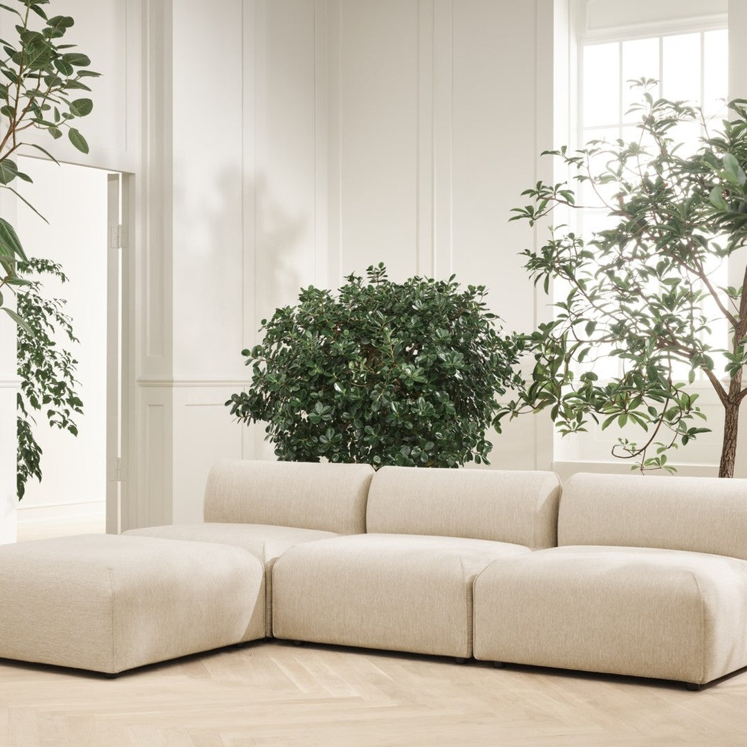 Beige sectional sofa with a smooth fabric texture, set against a light, airy interior and green leafy plants.