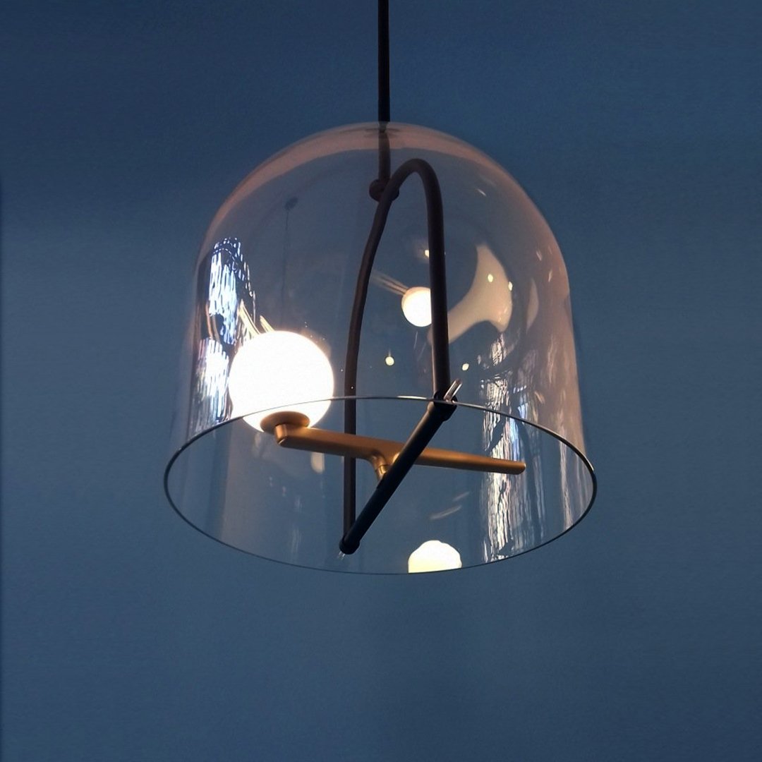 Clear glass pendant lamp with black accents and circular shapes, illuminated against a deep blue background.