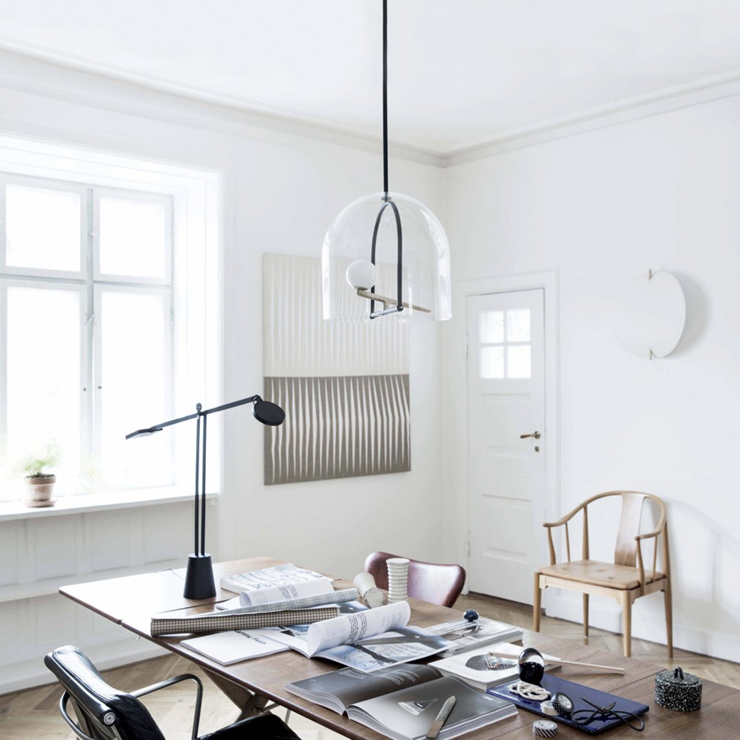 Clear glass pendant lamp with black accents, surrounded by a minimalist white and wood interior with subtle textural patterns.