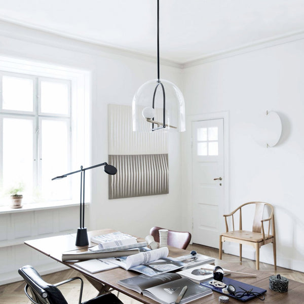 Clear glass pendant lamp with black accents, surrounded by a minimalist white and wood interior with subtle textural patterns.