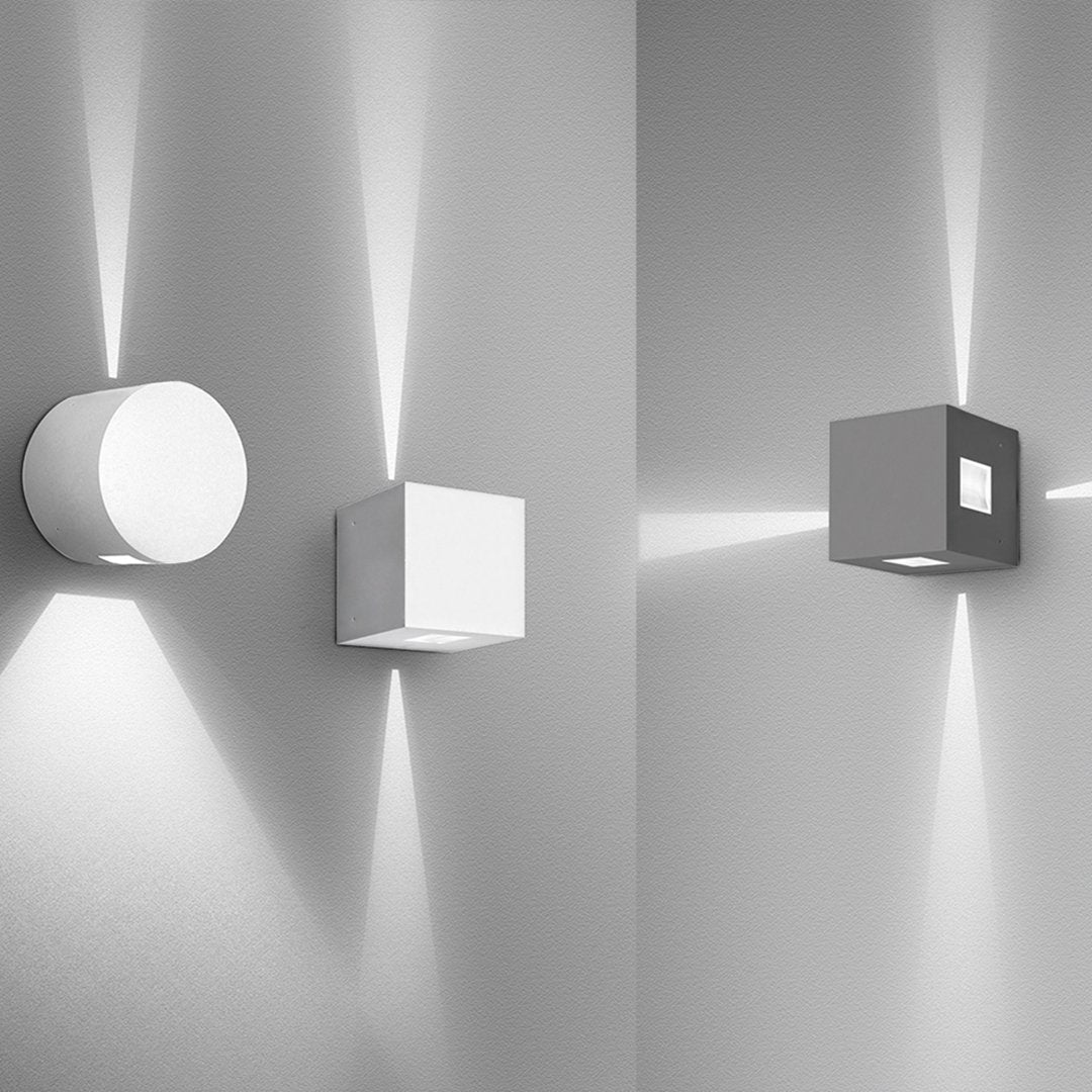 Two modern wall lights in sleek white and gray, featuring geometric shapes and soft light patterns on the wall.
