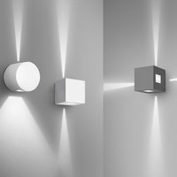 Two modern wall lights in sleek white and gray, featuring geometric shapes and soft light patterns on the wall.