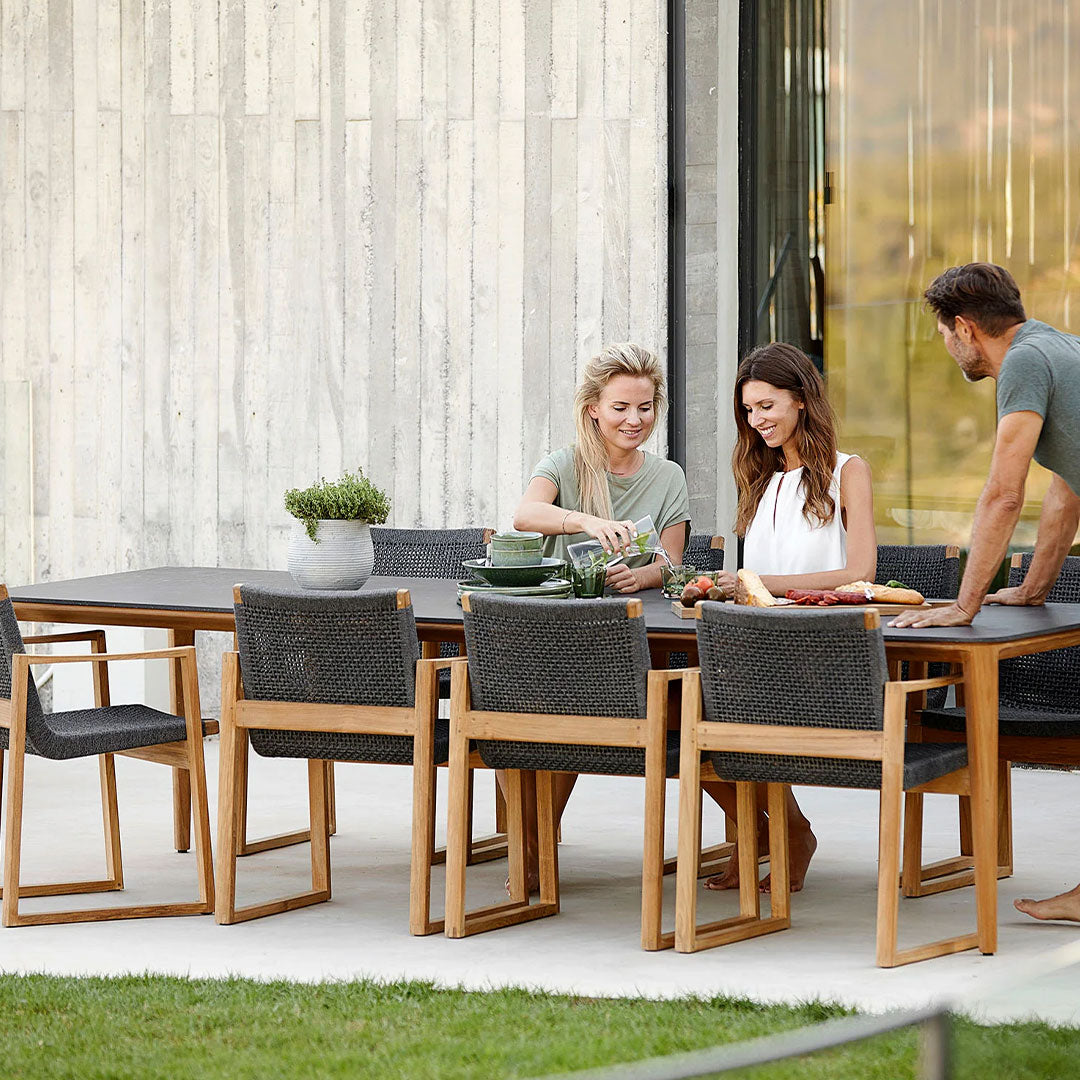 Outdoor dining set featuring natural wood tones, dark woven fabric chairs, and green dishware on a sleek table.