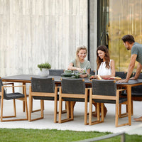Outdoor dining set featuring natural wood tones, dark woven fabric chairs, and green dishware on a sleek table.