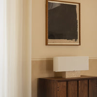 Textured white lamp on a wooden cabinet, featuring neutral wall colors and a dark abstract artwork above.