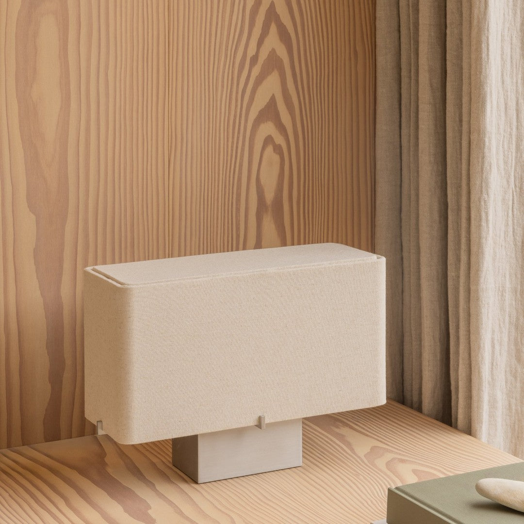 Beige fabric lamp with a minimalist design on a wooden surface, highlighting natural textures and warm tones.