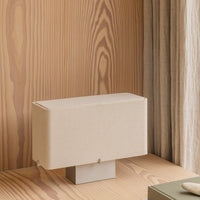 Beige fabric lamp with a minimalist design on a wooden surface, highlighting natural textures and warm tones.