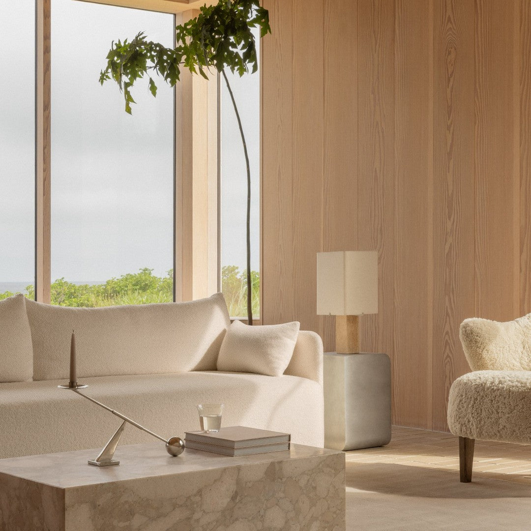 Light beige sofa and cream patterned armchair in a bright, minimalist room with wood walls and green foliage.