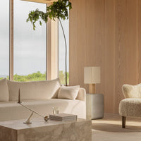 Light beige sofa and cream patterned armchair in a bright, minimalist room with wood walls and green foliage.