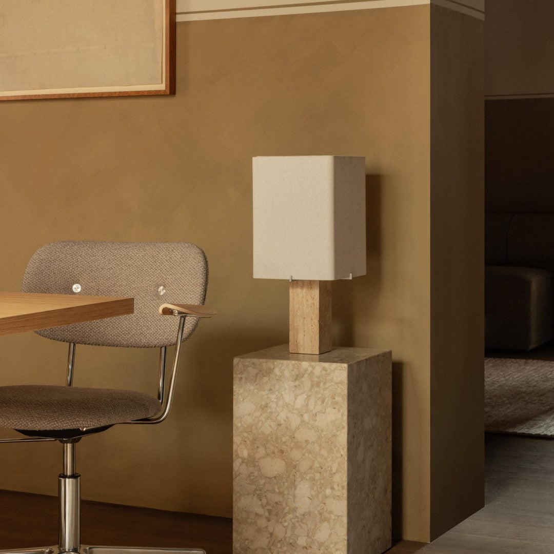 Minimalist beige lamp with a white shade, set on a textured stone base, against a warm brown wall.