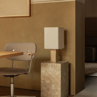 Minimalist beige lamp with a white shade, set on a textured stone base, against a warm brown wall.