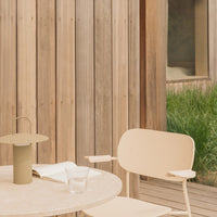 Beige modern chair and lamp on a light stone table, set against a rustic wooden wall and green grass backdrop.